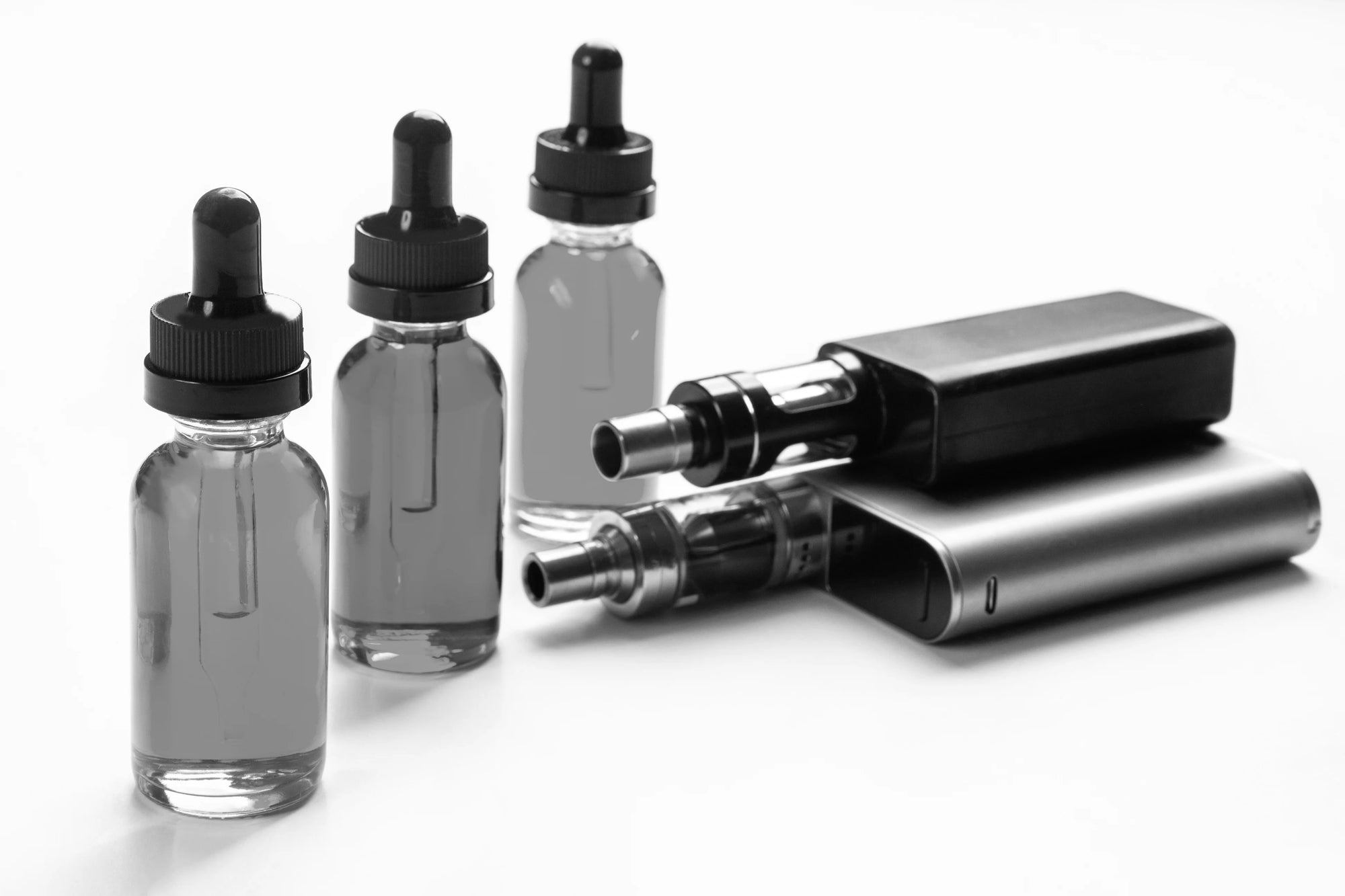 A black and white image of e-liquid bottles next to two vape kits
