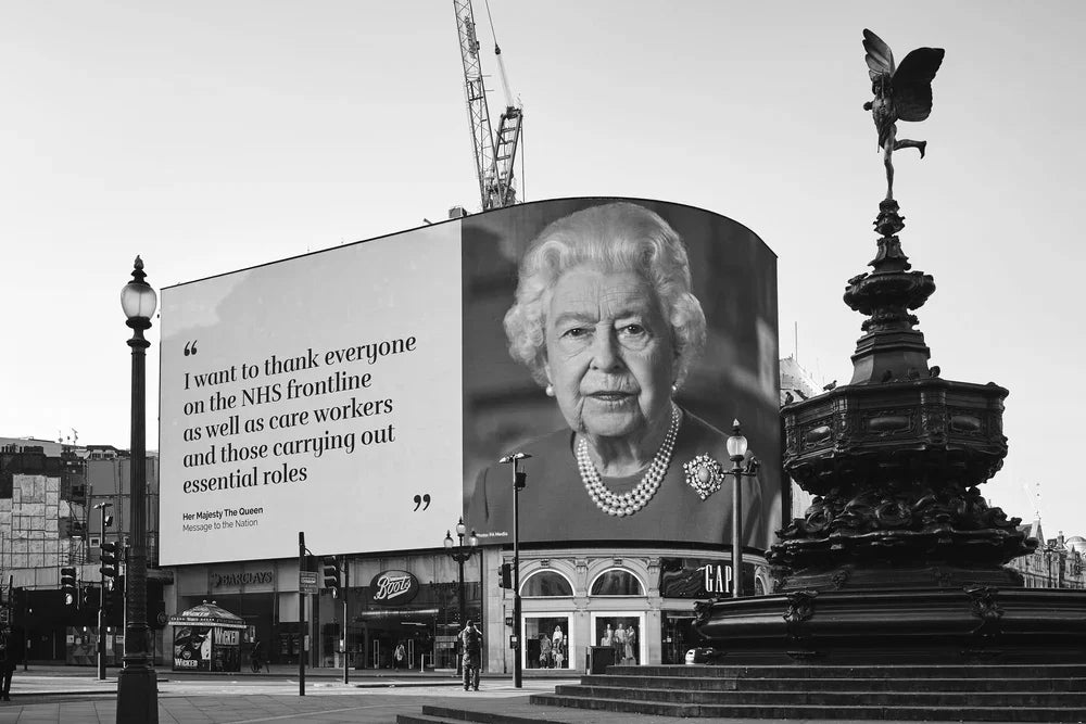 Large screen displaying a portrait of a the queen with a quote in an urban setting