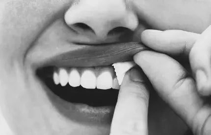 Black and white image of nicotine pouch being placed in mouth
