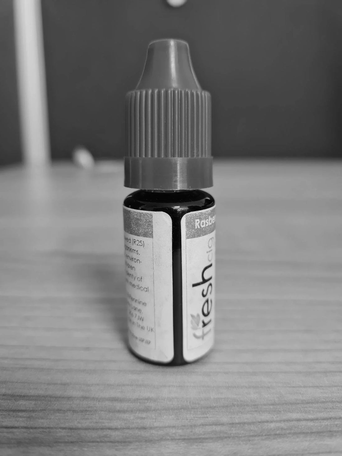 Small bottle labeled 'raspberry fresh' on a wooden surface with a blurred background