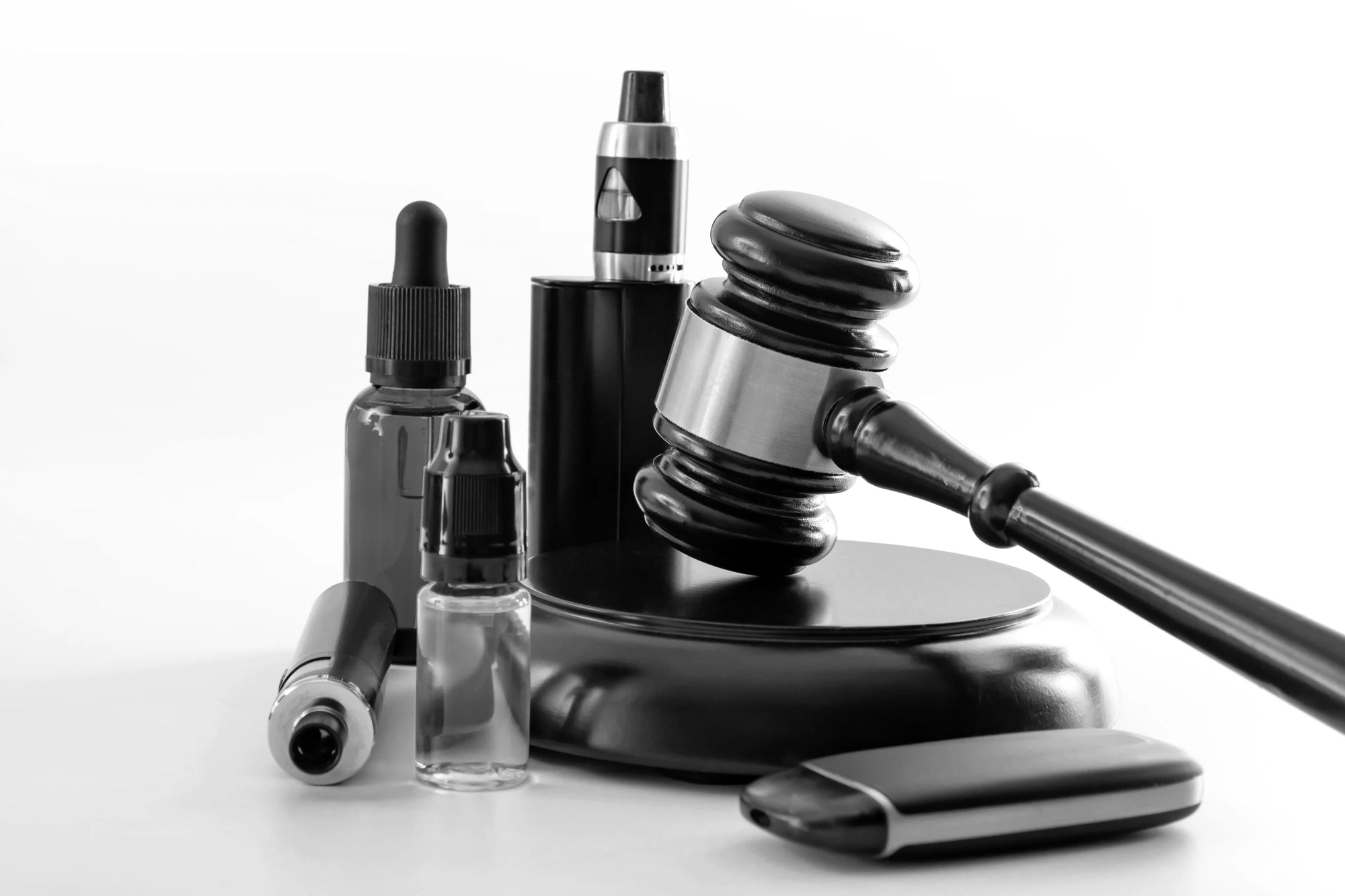 black and white image of a judge's gavel surrounded by vape products 